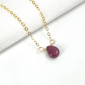 Könnte beinhalten: Eine zarte goldene Kettenkette mit einem einzelnen tropfenförmigen Rubin-Anhänger.