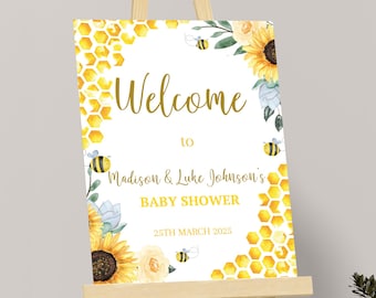 May include: A baby shower welcome sign on an easel. The sign features a watercolor design with sunflowers, bees, and honeycomb patterns. The text reads "Welcome to Madison & Luke Johnson's BABY SHOWER 25TH MARCH 2025."