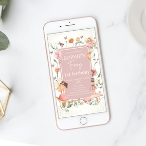 May include: A smartphone screen shows a digital invitation for Sophie's 1st birthday. The design is pink and white with floral and fairy illustrations. The text reads "Sophie's Fairy 1st birthday" with event details.