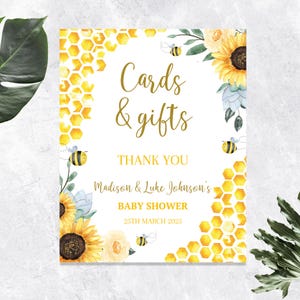 May include: A baby shower sign with a watercolor design. The sign features the text "Cards & Gifts" and "Thank You". The sign is decorated with sunflowers, bees, and honeycomb patterns. The baby shower is for Madison & Luke Johnson, March 25th, 2025.