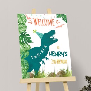 May include: A welcome sign for a second birthday party. The sign features a teal Tyrannosaurus Rex wearing a party hat, with the words "Welcome to Henry's 2nd Birthday". Green foliage and grass surround the text.