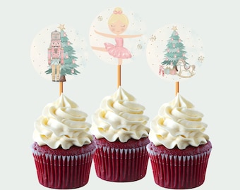 May include: Three red velvet cupcakes topped with white frosting, each adorned with a decorative topper. The toppers feature illustrations of a ballerina, a nutcracker, and a Christmas tree with gifts, creating a festive holiday theme.