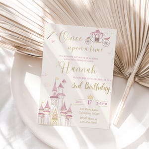 May include: A pink and gold princess-themed birthday invitation featuring a castle, carriage, and crown. The invitation reads "Once upon a time... In a kingdom not so far away lived a beautiful princess named Hannah. Please join us to celebrate her 3rd birthday. June 17, 2-5 PM. 123 Party Lane, California 56789. RSVP Mom at 123-456-7890."