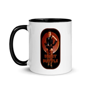 Puede incluir: Taza de café de cerámica blanca con borde negro. La taza presenta una ilustración colorida de un hombre con traje negro y tirantes rojos. El texto "Sweet Buttle" está escrito en una fuente de goteo.
