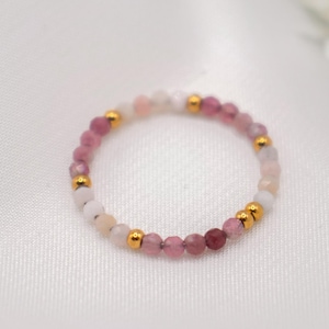 Könnte beinhalten: Ein zarter Ring aus rosa und weißen Perlen mit goldenen Akzenten. Der Ring besteht aus kleinen, runden Perlen und ist perfekt, um jedem Outfit einen Hauch von Farbe und Glanz zu verleihen.