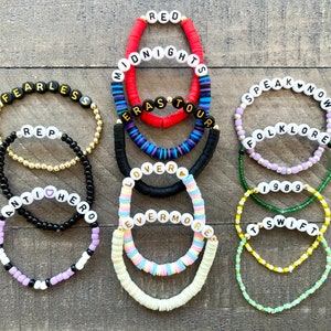 K&ouml;nnte beinhalten: Ein Set aus 10 bunten Perlenarmb&auml;ndern mit den Namen der Taylor Swift-Alben, darunter "Red", "Midnights", "Speak Now", "Folklore", "Lover", "Evermore", "Fearless", "1989", "Reputation" und "Taylor Swift".