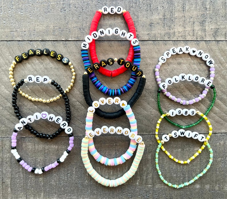 K&ouml;nnte beinhalten: Ein Set aus 10 bunten Perlenarmb&auml;ndern mit den Namen der Taylor Swift-Alben, darunter "Red", "Midnights", "Speak Now", "Folklore", "Lover", "Evermore", "Fearless", "1989", "Reputation" und "Taylor Swift".