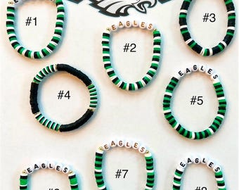 Könnte beinhalten: Acht grüne, weiße und schwarze Perlenarmbänder mit dem Wort "EAGLES" in goldenen Buchstaben. Jedes Armband ist von 1 bis 8 nummeriert.
