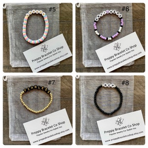 K&ouml;nnte beinhalten: Vier bunte Perlenarmb&auml;nder mit verschiedenen W&ouml;rtern, die darauf geschrieben sind. Die Armb&auml;nder werden auf wei&szlig;en Netzbeuteln mit einer Visitenkarte pr&auml;sentiert, auf der "Preppy Bracelet Co Shop" und eine Website-Adresse stehen. Die Armb&auml;nder sind mit 5, 6, 7 und 8 nummeriert.