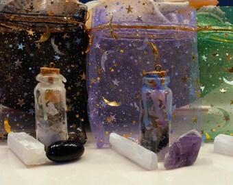 May include: Four small glass bottles filled with crystals and herbs, each in a different color organza bag with gold stars and moons. Each bottle is accompanied by a crystal, including a pink, white, purple, and green crystal.