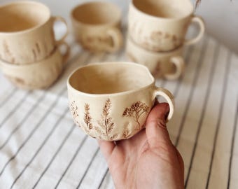 May include: A set of three ceramic mugs with a speckled, matte finish. Each mug features a different color: light blue, cream, and gray. The mugs have a simple, modern design and a comfortable handle. Perfect for coffee or tea.