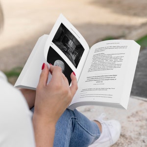 Puede incluir: Una persona sostiene un libro abierto con im&aacute;genes en blanco y negro y texto. Las p&aacute;ginas del libro son blancas, al igual que la portada. La persona lleva vaqueros azules y zapatillas blancas.