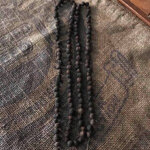 May include: A long strand of dark brown beads, possibly made of wood or clay, strung together on a thin thread. The beads are all roughly the same size and shape, and they have a slightly rough texture.