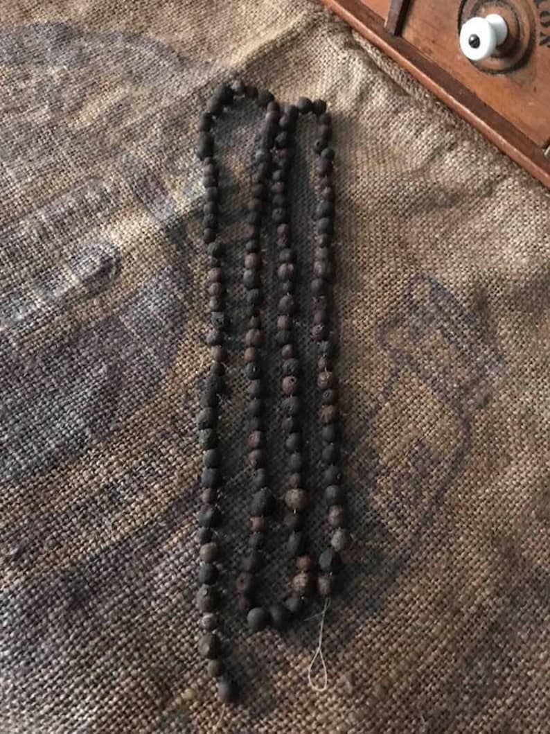 May include: A long strand of dark brown beads, possibly made of wood or clay, strung together on a thin thread. The beads are all roughly the same size and shape, and they have a slightly rough texture.