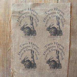 May include: Four burlap fabric squares with a black and white logo printed on each. The logo says "Two Hares Heirloom Variety Farm & Garden Seeds" with a picture of two rabbits. The bottom of each square says "Tuckerton, NJ 1817".