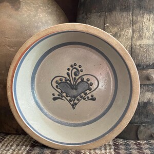 May include: A white ceramic bowl with a blue and brown heart design. The bowl has a light brown rim and a blue stripe around the edge.