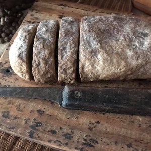 May include: A loaf of bread sliced on a wooden cutting board with a vintage knife. The bread is brown and crusty, and the knife is rusty.