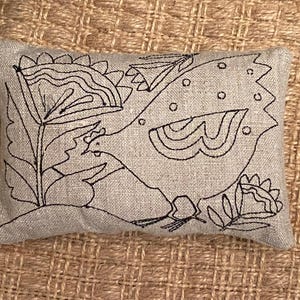 May include: A gray linen pillow with a black embroidered design of a bird and flowers.
