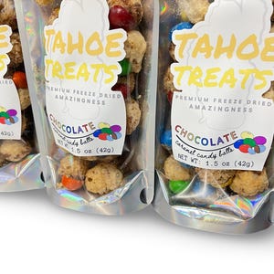 May include: Three clear plastic bags filled with freeze-dried chocolate caramel candy balls. Each bag has a label with the words "Tahoe Treats" in yellow, and "Chocolate caramel candy balls" below. The net weight is 1.5 oz (42g).