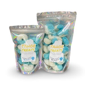 May include: Two bags of blue and white gummy rings. The smaller bag is labeled "TAHOE TREATS PREMIUM FREEZE DRIED AMAZINGNESS GUMMY RINGS BLUE RASPBERRY NET WT. 3 OZ (85g)". The larger bag is labeled "TAHOE TREATS PREMIUM FREEZE DRIED AMAZINGNESS GUMMY RINGS BLUE RASPBERRY NET WT. 5 OZ (140g)".