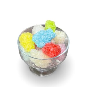 May include: A glass bowl filled with colorful, textured candy. The candy is in shades of blue, green, yellow, pink, and white.