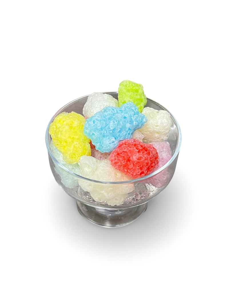 May include: A glass bowl filled with colorful, textured candy. The candy is in shades of blue, green, yellow, pink, and white.