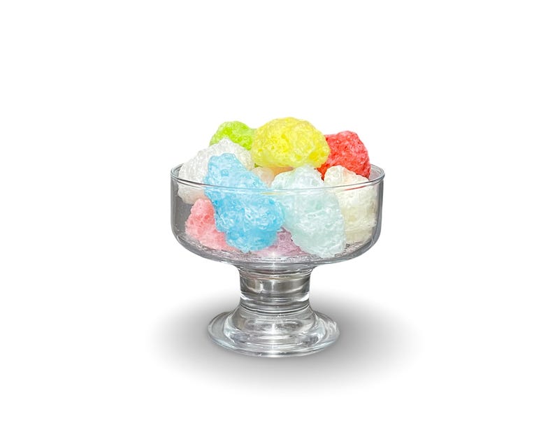 May include: A glass bowl filled with colorful candy. The candy is in the shape of small, irregular balls and is a mix of pink, blue, yellow, and white.