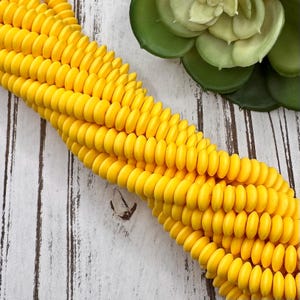 May include: A strand of bright yellow corn-shaped beads. The beads are smooth and glossy, resembling kernels of corn.