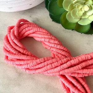 May include: A close-up of a pile of pink plastic beads. The beads are round and flat, and they are arranged in a circular pattern. The beads are perfect for making jewelry or other crafts.