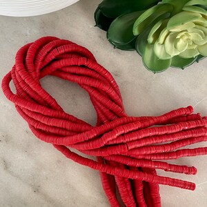 May include: A large quantity of red polymer clay beads, arranged in a loose pile. The beads are round and flat, with a slightly textured surface.
