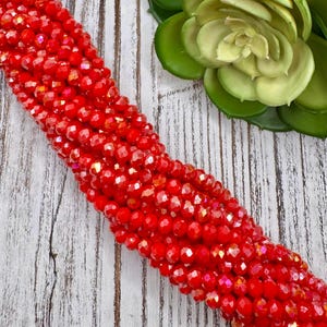 May include: A strand of red faceted glass beads. The beads are small and have a shiny, iridescent finish.