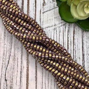 May include: A strand of brown and gold glass beads with white accents. The beads are small and round, and they are arranged in a spiral pattern.