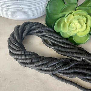 Op de afbeelding: Een streng zwarte rubberen kralen, elke kraal is een platte cirkel met een gat in het midden. De kralen zijn gerangschikt in een losse spiraal.