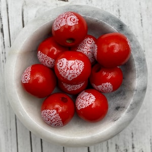 May include: A bowl of red wooden beads with white "I love you" lettering. The beads are round and have a smooth finish.