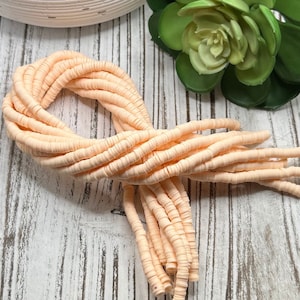 May include: A strand of peach-colored polymer clay beads. The beads are small and round, and they are strung together on a thin wire. The beads are arranged in a loose, flowing pattern.