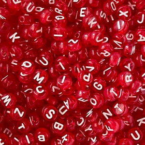 May include: A close-up image of a pile of red plastic alphabet beads. The beads are translucent and have white letters on them. The letters are all different and are randomly arranged.