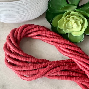 May include: A strand of red polymer clay beads. The beads are round and flat, and they are strung together in a long, continuous strand.