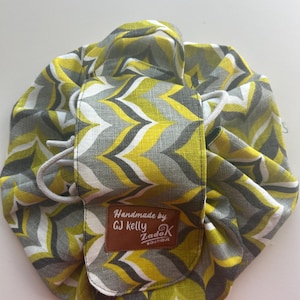 May include: A round, drawstring cosmetic bag with a yellow, grey, and white chevron pattern. The bag has a brown leatherette label that reads "Handmade by GJ Kelly ZadaK Boutique."