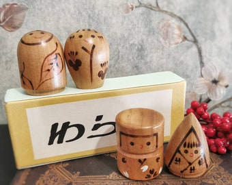 May include: Four wooden figurines with painted details. The figurines are in the shape of people with different designs. The figurines are on a box with the word "から" written on it.