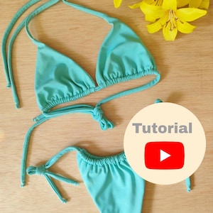 Puede incluir: Un top y una parte inferior de bikini turquesa con tirantes ajustables. El top es de estilo triangular y la parte inferior es de estilo atrevido. La imagen incluye el texto "Tutorial" con un icono de botón de reproducción.