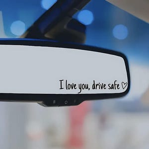 以下が含まれることがあります： 「愛してる、安全運転で」というメッセージが黒のマジックで書かれた、ハートが描かれたリアビューミラーです。