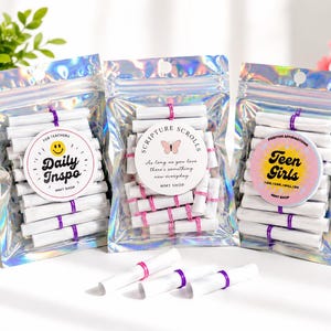 Può includere: Tre bustine olografiche contenenti piccoli rotoli di carta bianca legati con fascette rosa o viola. Ogni bustina presenta un'etichetta circolare: Daily Inspo con una faccina sorridente, Scripture Scrolls con una farfalla e Teen Girls con un sole.