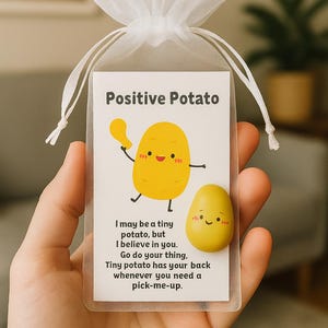 May include: A small, clear mesh bag tied with a white ribbon, containing a card and a yellow potato-shaped charm. The card reads "Positive Potato" with a cartoon potato illustration and inspirational text.