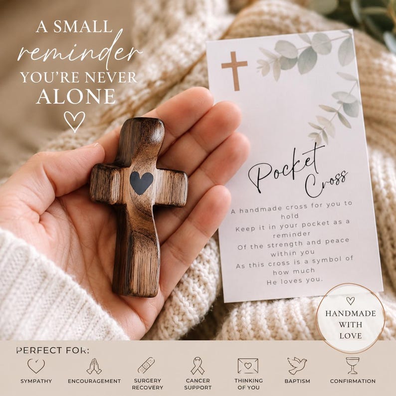 May include: A small dark brown wooden pocket cross with a black heart icon in the center. Beside it is a white card with the text Pocket Cross, a small cross symbol, and eucalyptus illustrations, along with the text A small reminder you're never alone.