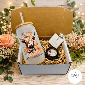 May include: A gift box containing a frosted glass tumbler with a bamboo lid and straw, featuring a highland cow and floral graphic with the text Life is better with fluffy cows, alongside a small candle and a tag reading A little something for you.