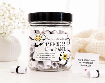 May include: A clear glass jar with a black lid, filled with rolled-up white notes. The jar has a label that reads "The Just-Because Jar HAPPINESS IS A HABIT." A small card reads "YOU'VE SURVIVED 100% OF YOUR BAD DAYS. SOLID RECORD."