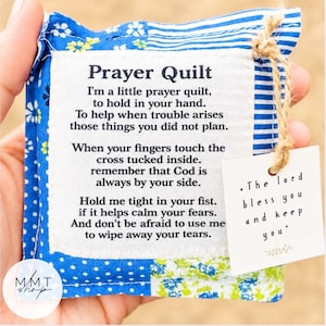 May include: A small, square prayer quilt with blue and white floral and striped fabric. The quilt has a white label with the text "Prayer Quilt" and a poem. A smaller tag reads "The lord bless you and keep you."