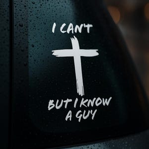 Può includere: Adesivo per finestrino auto nero con croce bianca e testo "I CAN'T BUT I KNOW A GUY". Gocce d'acqua creano una texture sul finestrino.