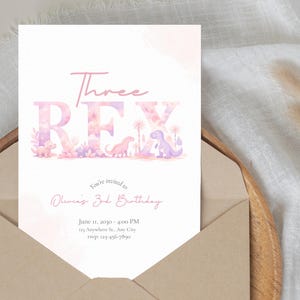 May include: A light pink birthday invitation card with the text "Three REX" in a playful font, featuring dinosaur illustrations. The card is inside a brown envelope, with additional text inviting guests to Olivia's 3rd birthday.