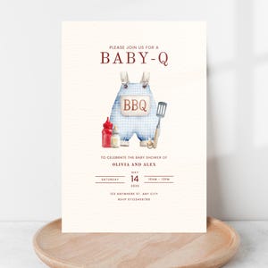 May include: Baby shower invitation with a watercolor illustration of blue gingham overalls with the word "BBQ". The invitation includes the text "PLEASE JOIN US FOR A BABY-Q" and details for Olivia and Alex's baby shower.